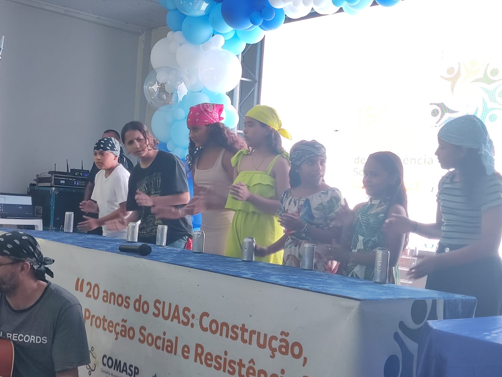 Crianças e adolescentes tocando latinhas como instrumentos de percussão durante apresentação cultural na conferência